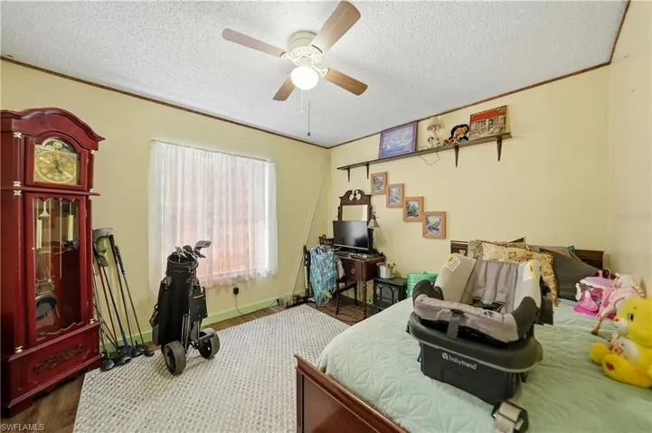 Bedroom with ceiling fan, crown molding, dark wood-style floors, and a textured ceiling