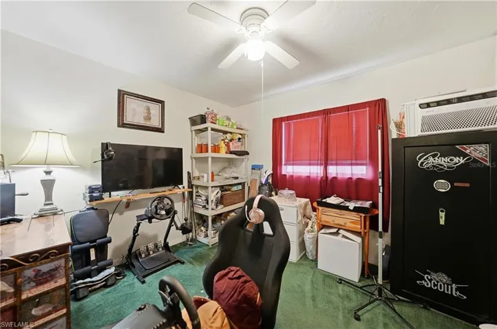 Carpeted office featuring a wall unit AC and a ceiling fan