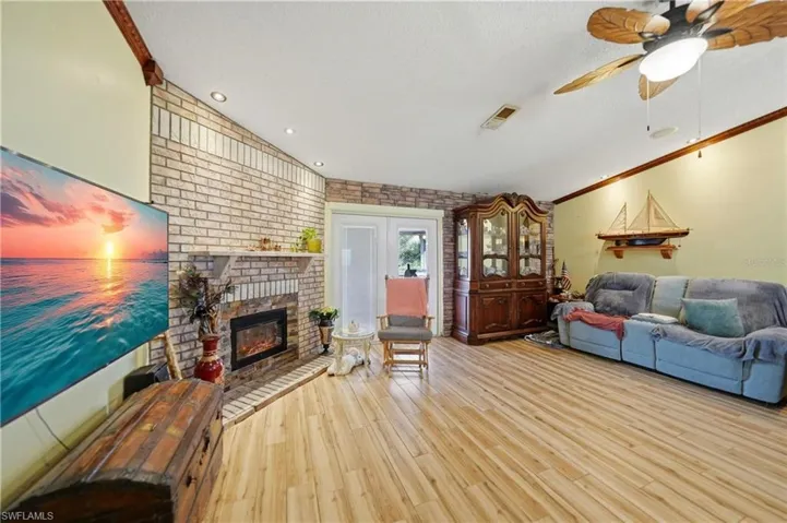 Living room with ornamental molding, wood finished floors, brick wall, a ceiling fan, and a fireplace