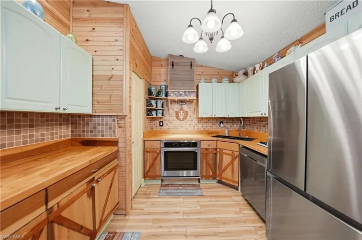 Kitchen with stainless steel appliances, open shelves, butcher block counters, light wood-style flooring, and pendant lighting