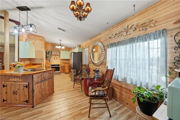 Dining room featuring wooden walls, light wood-style flooring, a chandelier, a textured ceiling, and lofted ceiling