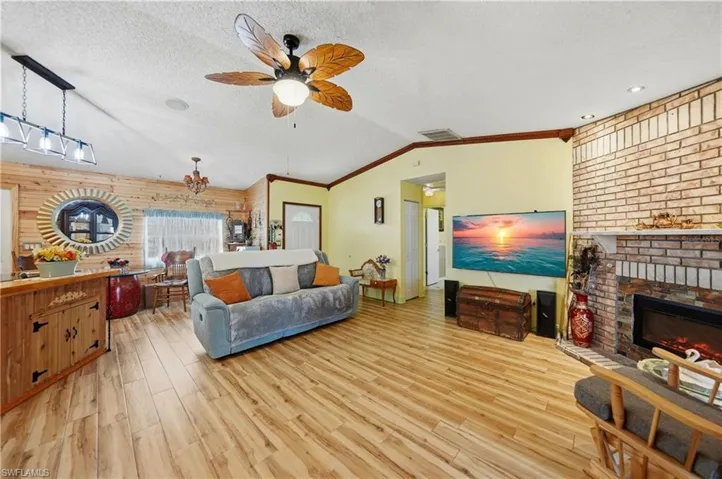 Living area with ornamental molding, a brick fireplace, a textured ceiling, light wood-style floors, and vaulted ceiling