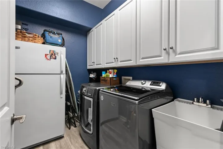 Laundry area featuring a textured wall, separate washer and dryer, light wood-style floors, and cabinet space