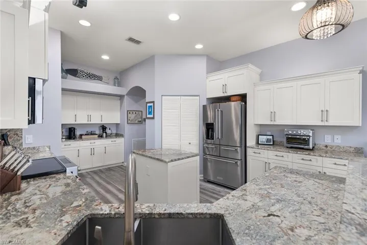 Kitchen featuring high quality fridge, light stone countertops, white cabinets, a kitchen island, and light wood-type flooring