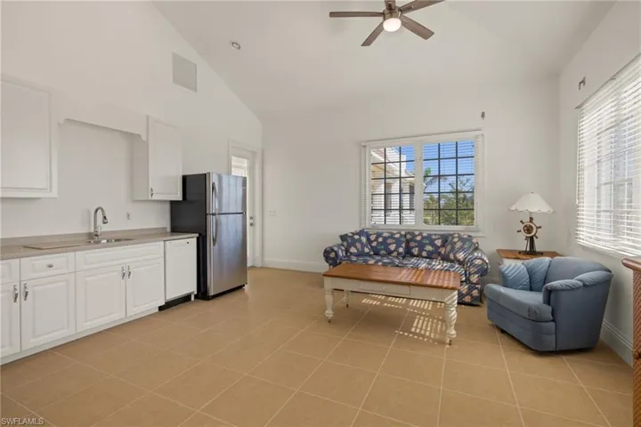 Living room with high vaulted ceiling, ceiling fan, light tile patterned flooring, and a healthy amount of sunlight