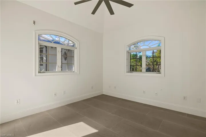 Empty room with ceiling fan, dark tile patterned floors, and vaulted ceiling