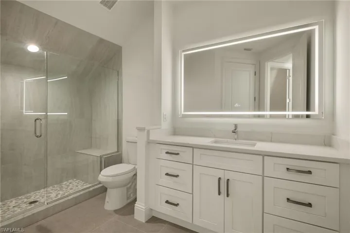 Bathroom featuring tile patterned flooring, toilet, vanity, and a shower with shower door