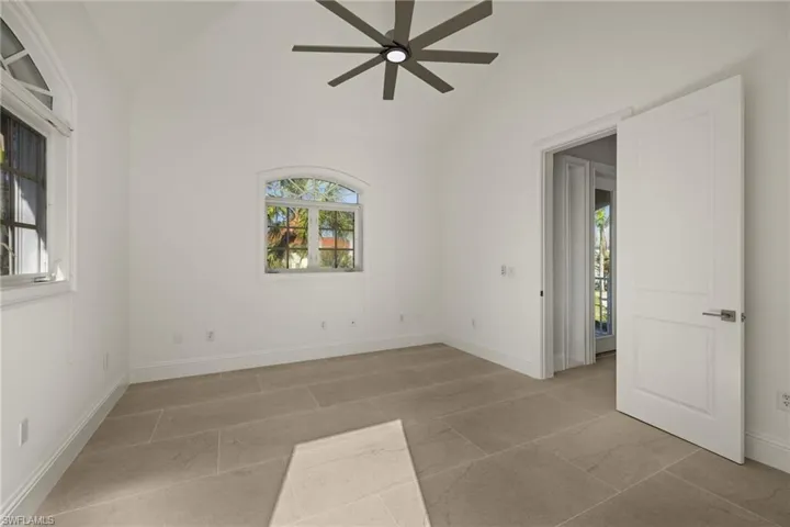 Empty room with high vaulted ceiling, ceiling fan, and a wealth of natural light