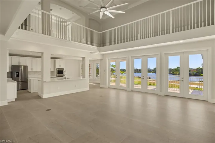 Unfurnished living room with a high ceiling, ceiling fan, french doors, and a water view