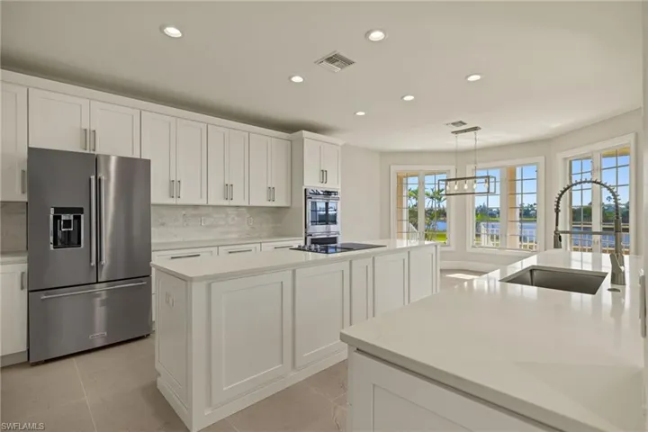 Kitchen featuring a kitchen island with sink, appliances with stainless steel finishes, hanging light fixtures, sink, and white cabinetry