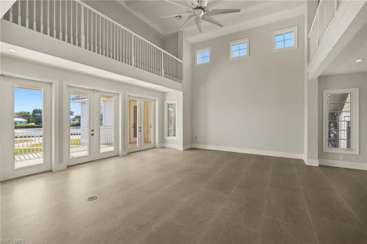 Unfurnished living room with a towering ceiling, ceiling fan, and french doors