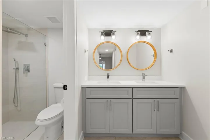 Bathroom with dual vanity, toilet, a tile shower, and tile patterned flooring