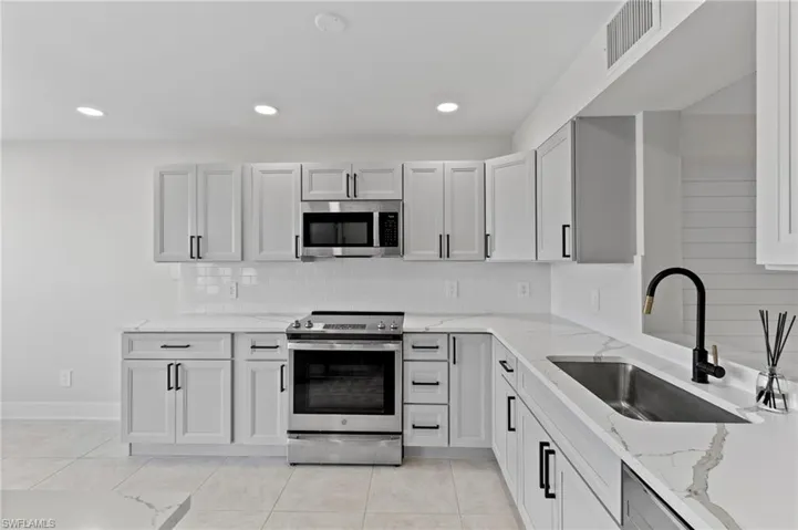 Kitchen featuring sink, light stone countertops, light tile patterned floors, and stainless steel appliances