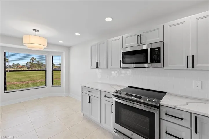 Kitchen with stainless steel appliances, pendant lighting, light stone countertops, light tile patterned floors, and backsplash