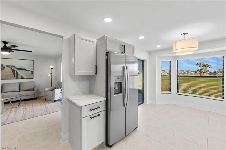 Kitchen with ceiling fan, hanging light fixtures, light stone countertops, stainless steel fridge, and light tile patterned floors