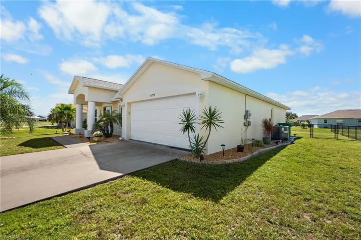 Stucco exterior featuring a two-car garage, covered entryway with structural columns, concrete driveway, and a chain-link fenced backyard