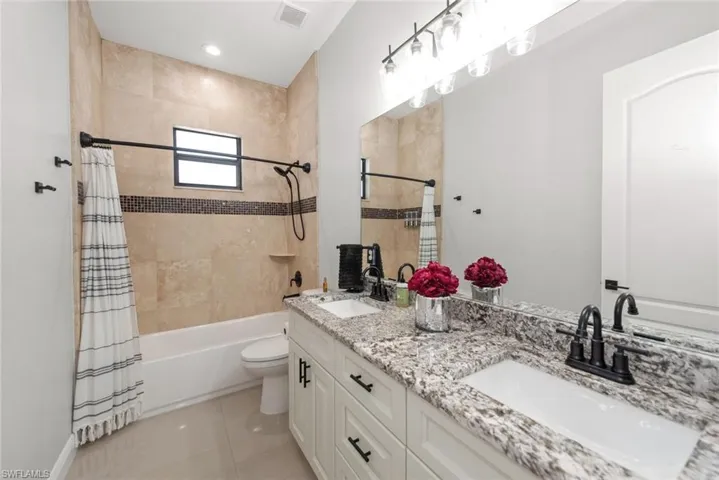Bathroom featuring double vanity, shower / bath combo with shower curtain, and light tile patterned flooring