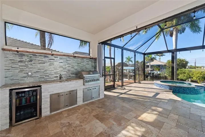 View of patio with a sunroom, glass enclosure, a pool with connected hot tub, beverage cooler, and an outdoor kitchen