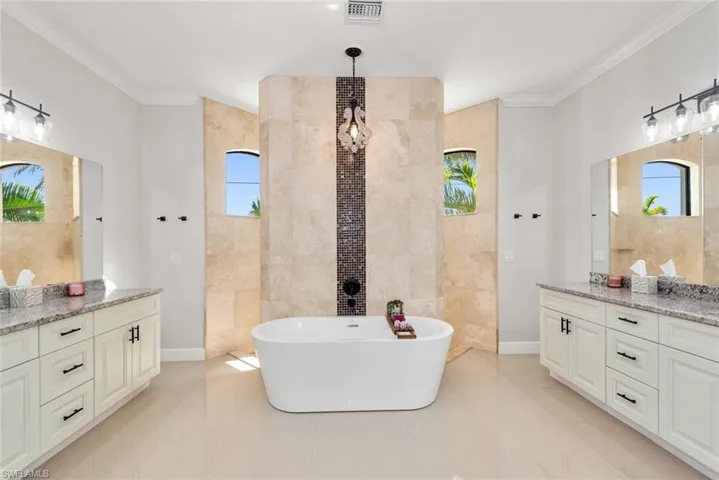 Bathroom with a freestanding bath, a walk in shower, plenty of natural light, two vanities, and ornamental molding