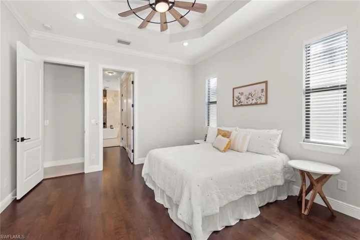 Bedroom featuring recessed lighting, a tray ceiling, ornamental molding, ensuite bathroom, and dark wood-type flooring