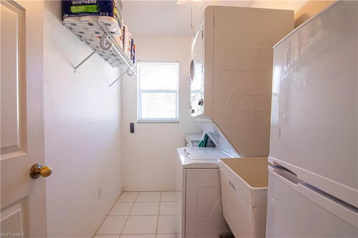 Clothes washing area with stacked washing maching and dryer, sink, and light tile patterned floors