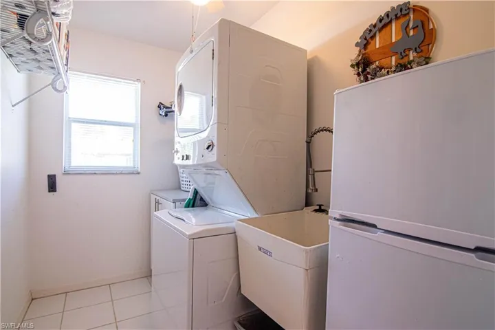 Laundry room with light tile patterned floors, stacked washing maching and dryer, and sink