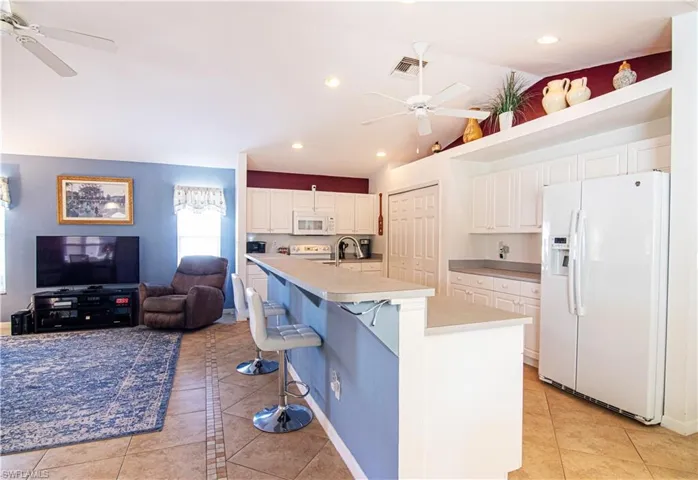 Kitchen featuring white cabinetry, a large island, lofted ceiling, white appliances, and a breakfast bar area