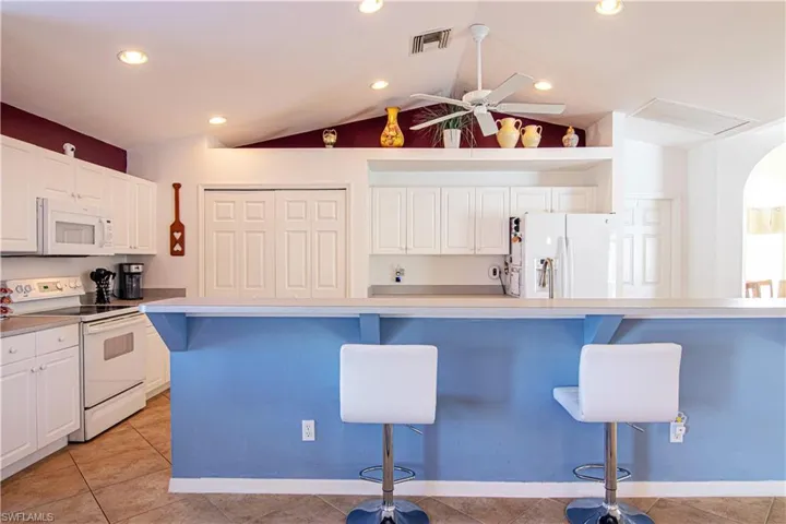 Kitchen with a kitchen bar, white appliances, white cabinets, and lofted ceiling
