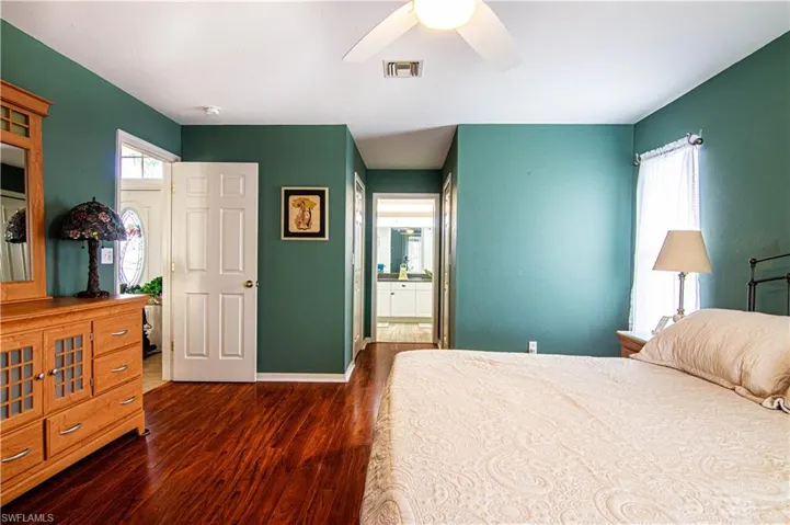 Bedroom with connected bathroom, multiple windows, ceiling fan, and dark hardwood / wood-style flooring