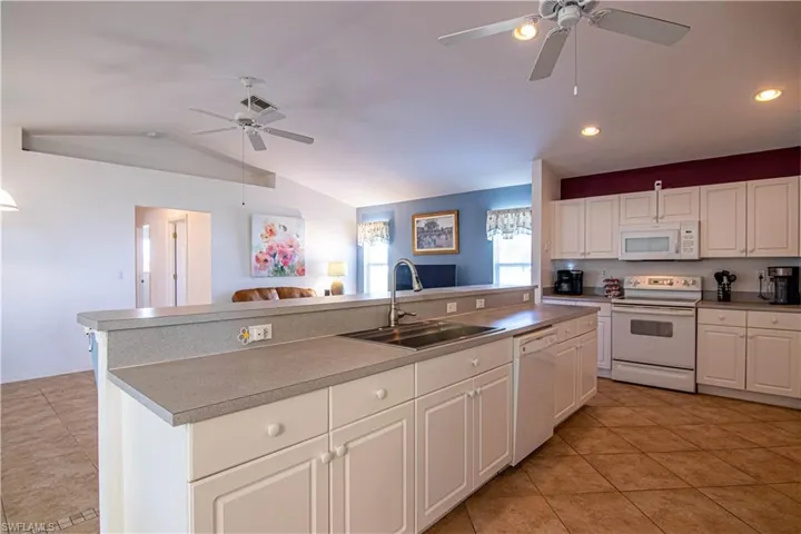Kitchen featuring vaulted ceiling, sink, white cabinets, and white appliances
