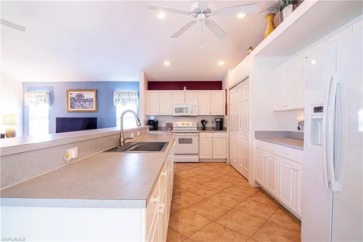Kitchen featuring white appliances, white cabinets, sink, ceiling fan, and light tile patterned floors