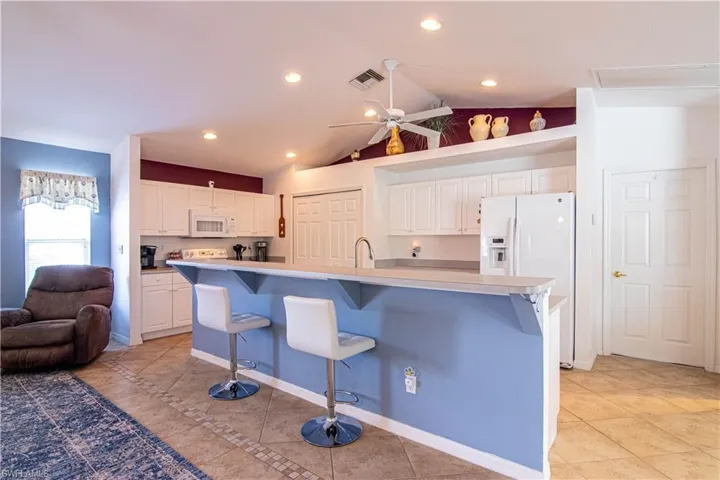 Kitchen featuring a breakfast bar, white appliances, white cabinets, a spacious island, and light tile patterned floors
