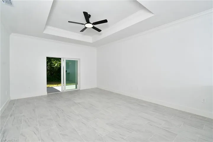 Recessed tray ceiling with crown molding and a ceiling fan, white walls, and large format tile flooring