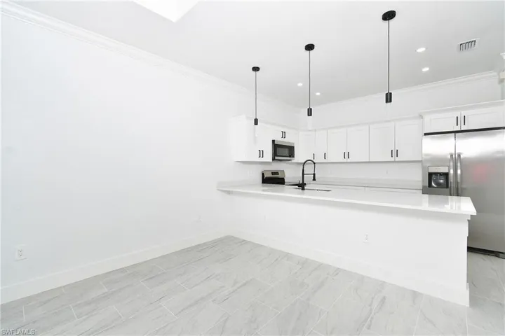 Contemporary kitchen featuring white cabinetry, stainless steel appliances, a breakfast bar, pendant lighting, and light-toned tile flooring
