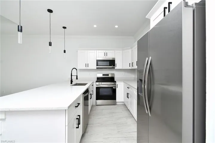 Kitchen featuring white cabinetry, stainless steel appliances, white countertops, and pendant lighting