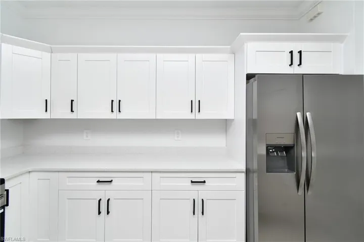 White shaker-style cabinetry with matte black hardware, light-toned countertops, and a built-in stainless steel refrigerator
