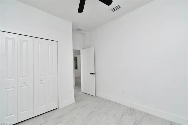 White paneled bi-fold closet doors, light-toned tile flooring, and a black ceiling fan