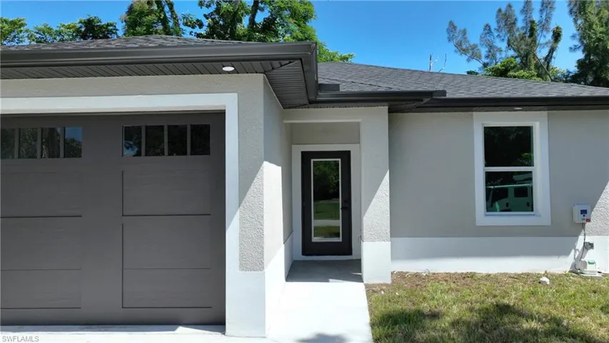 Modern exterior with a neutral stucco finish, dark gray garage door with windows, black-framed front entry door, and white-framed windows
