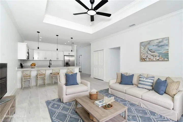 Bright open-concept living space with a recessed tray ceiling, ceiling fan, and light-toned tile flooring