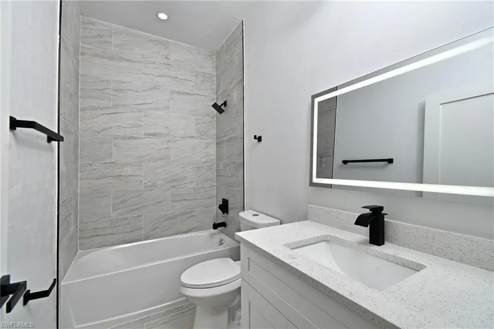 Bathroom featuring a vanity with an integrated sink, solid surface countertop, matte black faucet, and an illuminated mirror