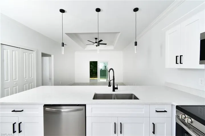 White shaker cabinetry with black hardware, stainless steel appliances, dual-basin sink with gooseneck faucet, light-toned countertops, and recessed ceiling with a fan