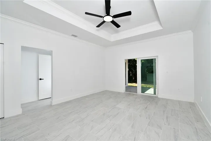 Tray ceiling with crown molding, ceiling fan with integrated lighting, sliding glass door, white interior door with black hardware, and large format tile flooring