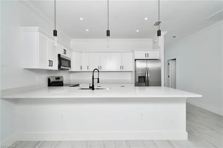 White kitchen featuring an island with a sink, stainless steel appliances, recessed lighting, and pendant lighting fixtures