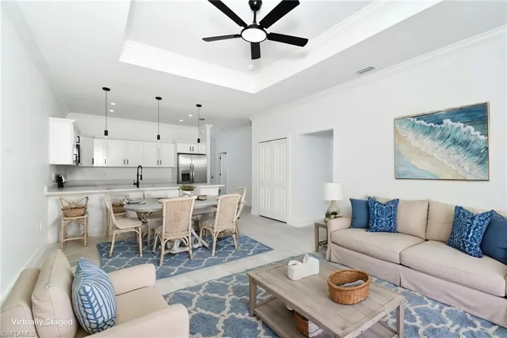 Open-concept living space featuring a tray ceiling with a ceiling fan, white kitchen cabinetry, stainless steel appliances, and a built-in kitchen island