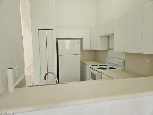 Kitchen with white cabinetry, kitchen peninsula, a towering ceiling, light tile patterned flooring, and white appliances