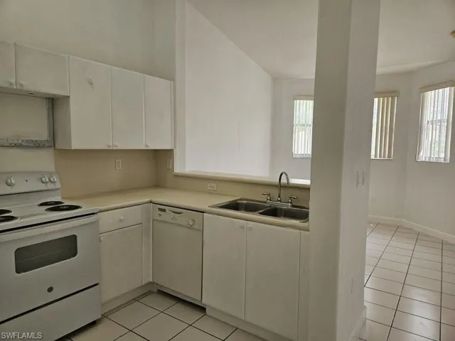 Kitchen featuring light tile patterned floors, white appliances, sink, and a healthy amount of sunlight
