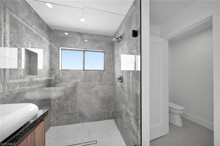 Bathroom with vanity, a marble finish shower, and toilet