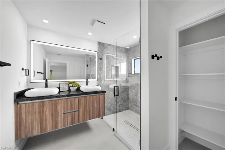 Bathroom with a sink, a shower stall, double vanity, and a spacious closet