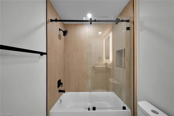 Full bathroom with toilet and shower / bath combination with glass door