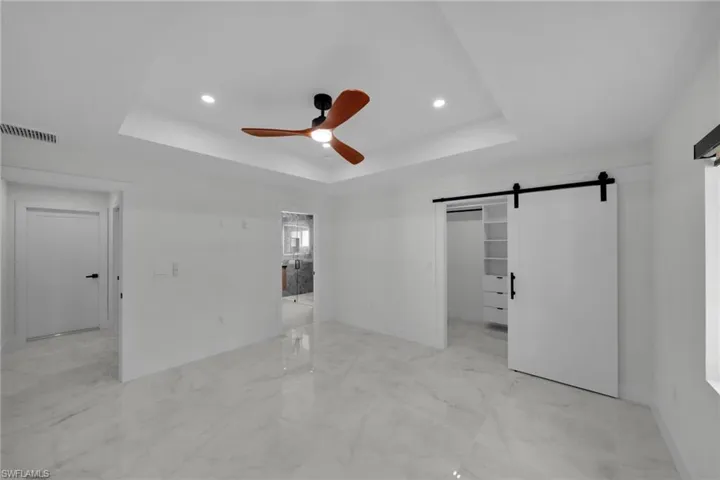 Unfurnished bedroom with baseboards, a tray ceiling, a barn door, and visible vents